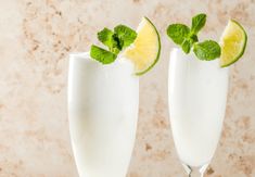 two glasses filled with white liquid and garnished with limes