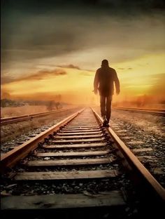 a man walking on train tracks towards the sun