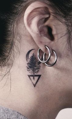 a woman's neck with a small tree and two hoop tattoos on her left ear