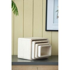 three stacked white square objects sitting on top of a shelf next to a plant in a black frame