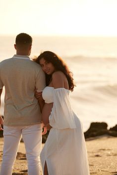 a man standing next to a woman on top of a sandy beach near the ocean