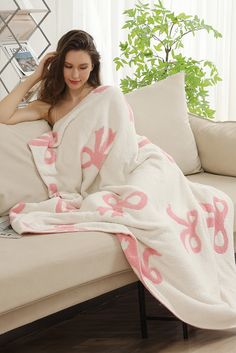 a woman sitting on a couch under a pink and white blanket