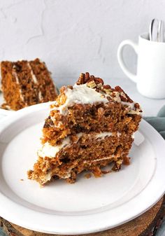 a piece of carrot cake on a plate with a fork and cup in the background