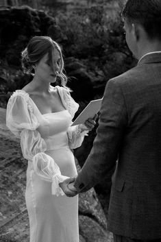 a pregnant woman in a white dress standing next to a man holding a piece of paper