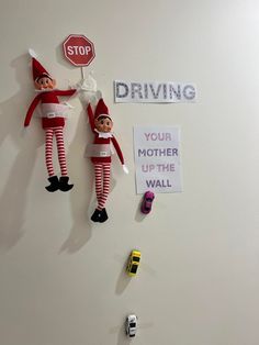 two elfs hanging on the wall with signs and magnets attached to them that read driving your mother up the wall