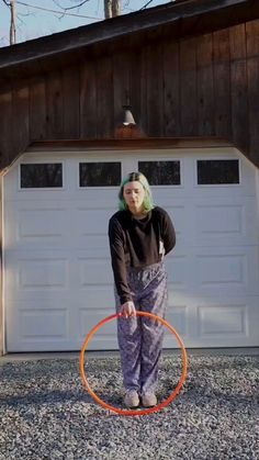 a woman is standing in front of a garage with an orange hula hoop