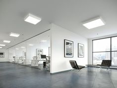 an empty room with chairs and pictures on the wall in front of large glass windows