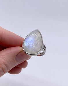 This is a large teardrop shape Rainbow Moonstone ring. The setting and band are sterling silver, with white gold coating on top. This stone has a lovely iridescent blue shimmer as the light hits it, and the ring has a secure bezel setting with a delicate cut out detail along the sides of the band. The ring size is #7.75.  Please let us know if you have any questions. Stone hardness 6-6.5 / Source: Sri Lanka, India, Brazil, USA Rainbow Moonstone is a type of feldspar; the sheen is caused by light Large Moonstone Ring, Teardrop Ring, Iridescent Blue, Rainbow Moonstone Ring, Moonstone Ring, Rainbow Moonstone, Bezel Setting, Rings Statement, Sri Lanka