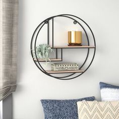 a round metal shelf with two candles on it next to pillows and a window sill