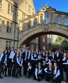 a group of young people in school uniforms posing for a photo under an arched bridge