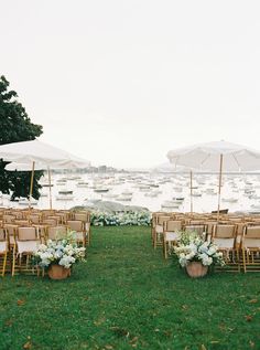 chairs and umbrellas are set up in the grass for an outdoor ceremony at a lake