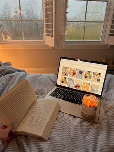 an open book sitting on top of a bed next to a laptop computer and candle