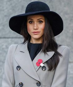 a woman wearing a gray coat and black hat with a poppy on the lapel