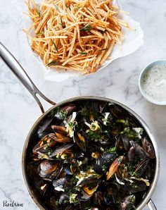 a pan filled with mussels next to a bowl of fries