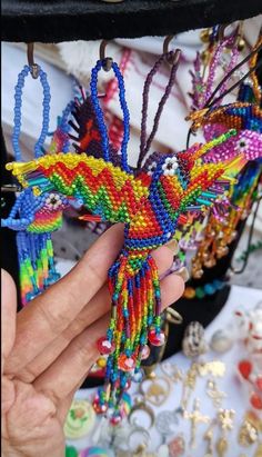 a person holding a colorful beaded bird ornament in their left hand, with other beads and jewelry on the table