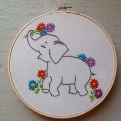 an elephant with flowers on it's head is embroidered onto a hoop hanging from a wall