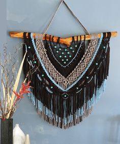 a wall hanging made out of wood sticks and beaded fringes on a blue wall