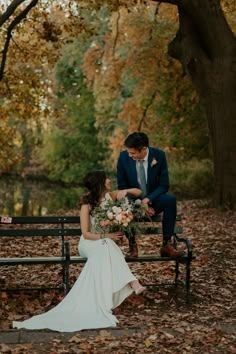 a bride and groom sitting on a bench in the woods with leaves all around them