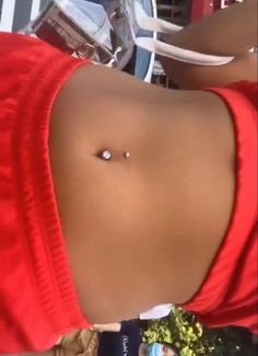 a close up of a person wearing a red shirt with a piercing on their stomach