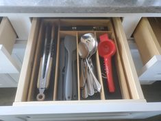 an open drawer with utensils and spoons in it on top of a counter