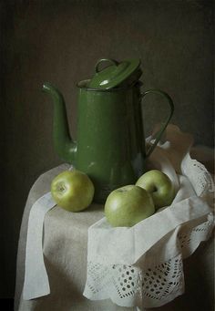 a green teapot sitting on top of a table next to two apples and a lace doily