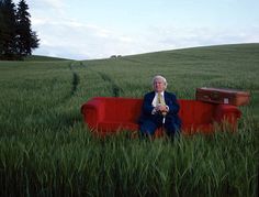 an old man sitting on a red couch in tall grass