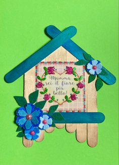 a house made out of popsicle sticks with flowers on the outside and a blue ribbon hanging from it