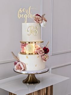 a three tiered wedding cake with flowers on top and gold lettering that says best begins