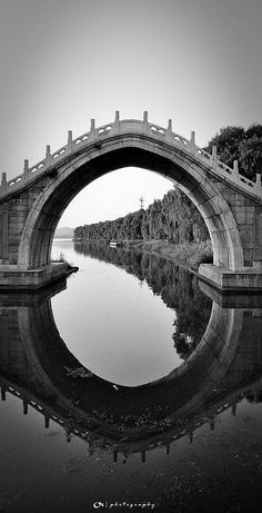 an arched bridge over water with trees in the background