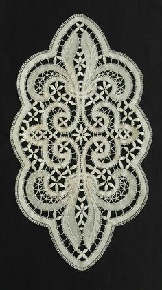 a white doily with an intricate design on the side and black fabric behind it