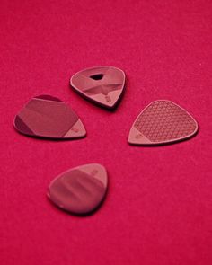 four guitar picks sitting on top of a pink surface