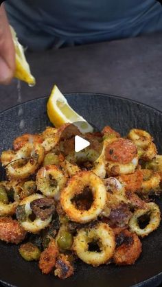 a black plate topped with fried food next to a lemon wedge