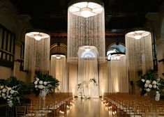 an indoor wedding venue with tall chandeliers and white flowers on the aisle line