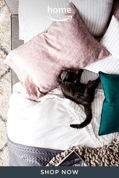 a black cat laying on top of a bed next to pillows and pillowcases