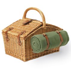 a wicker picnic basket with green blanket and matching napkins on the handle, sitting next to a rolled up towel