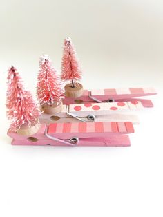 small pink trees are sitting on top of clothes pegs with scissors and paper clips