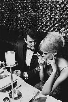 a man and woman sitting at a table with food in front of them, talking on the phone