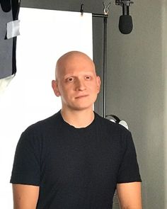 a bald man standing in front of a camera