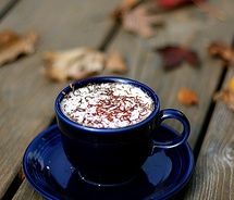 a cup of hot chocolate sitting on top of a blue saucer next to leaves