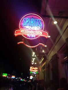 the sign for spirits bar and grill is lit up at night with people walking by