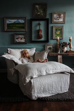 a woman laying on top of a white bed in a room with blue walls and pictures