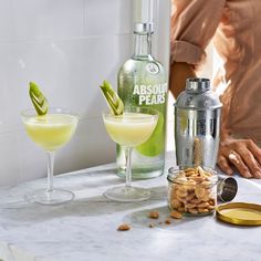 two glasses filled with alcoholic drinks on top of a counter next to a shaker