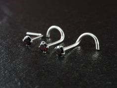 two pairs of silver earrings with garnetia stones on them sitting on a black surface