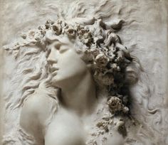 a white statue with flowers on it's head and hair blowing in the wind