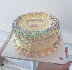 a cake with flowers and hearts on it being held by a woman's hand