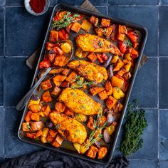 a pan filled with chicken and vegetables on top of a blue tile floor next to a knife