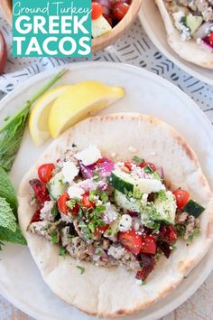 a taco with meat, tomatoes and cucumbers on it next to a lemon wedge