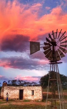 a windmill sitting in the middle of a field next to a building with a red sky behind it