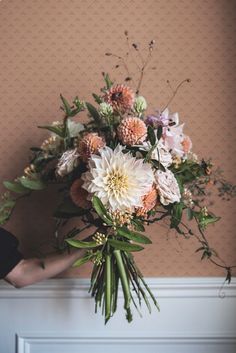 a person holding a bouquet of flowers in front of a wall with pink and white flowers