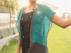 a woman standing in front of a park bench wearing a crocheted shawl